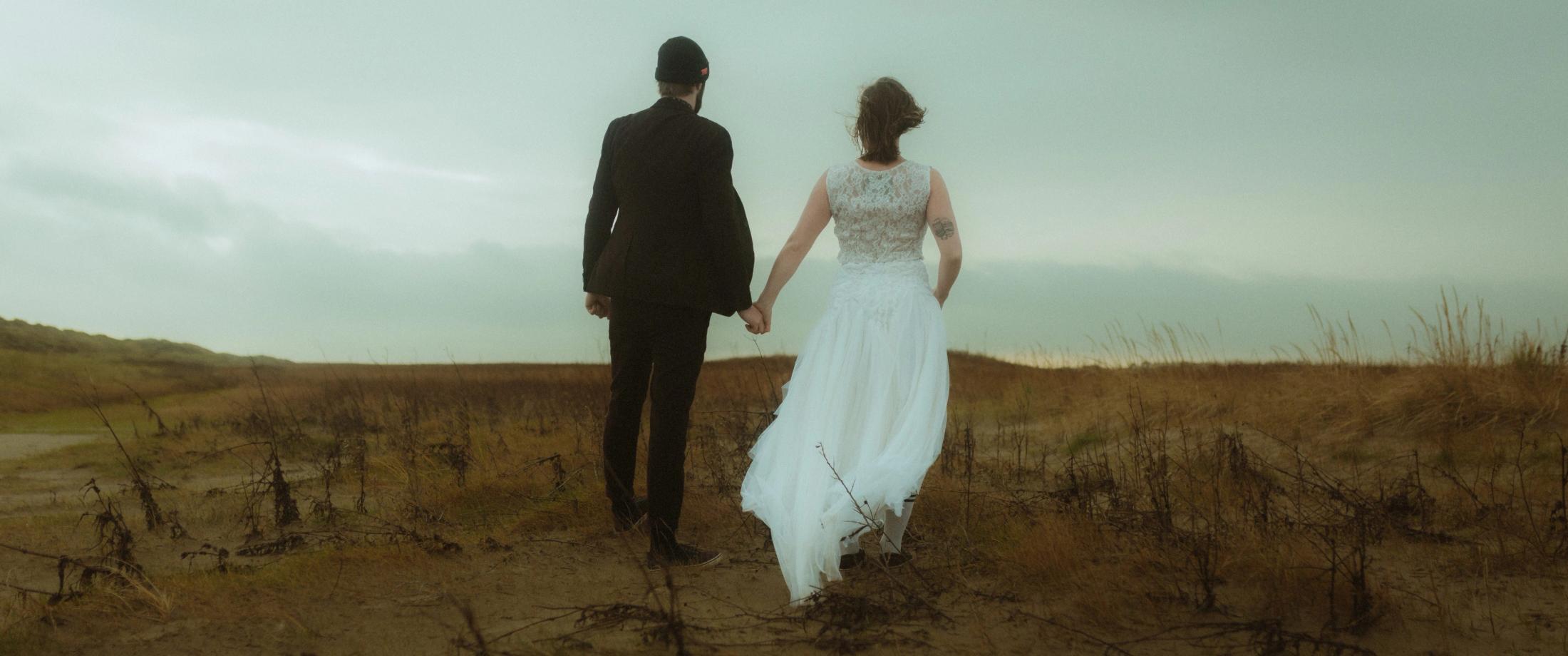 Anni and Daniel walk away hand in hand across the open dunes.