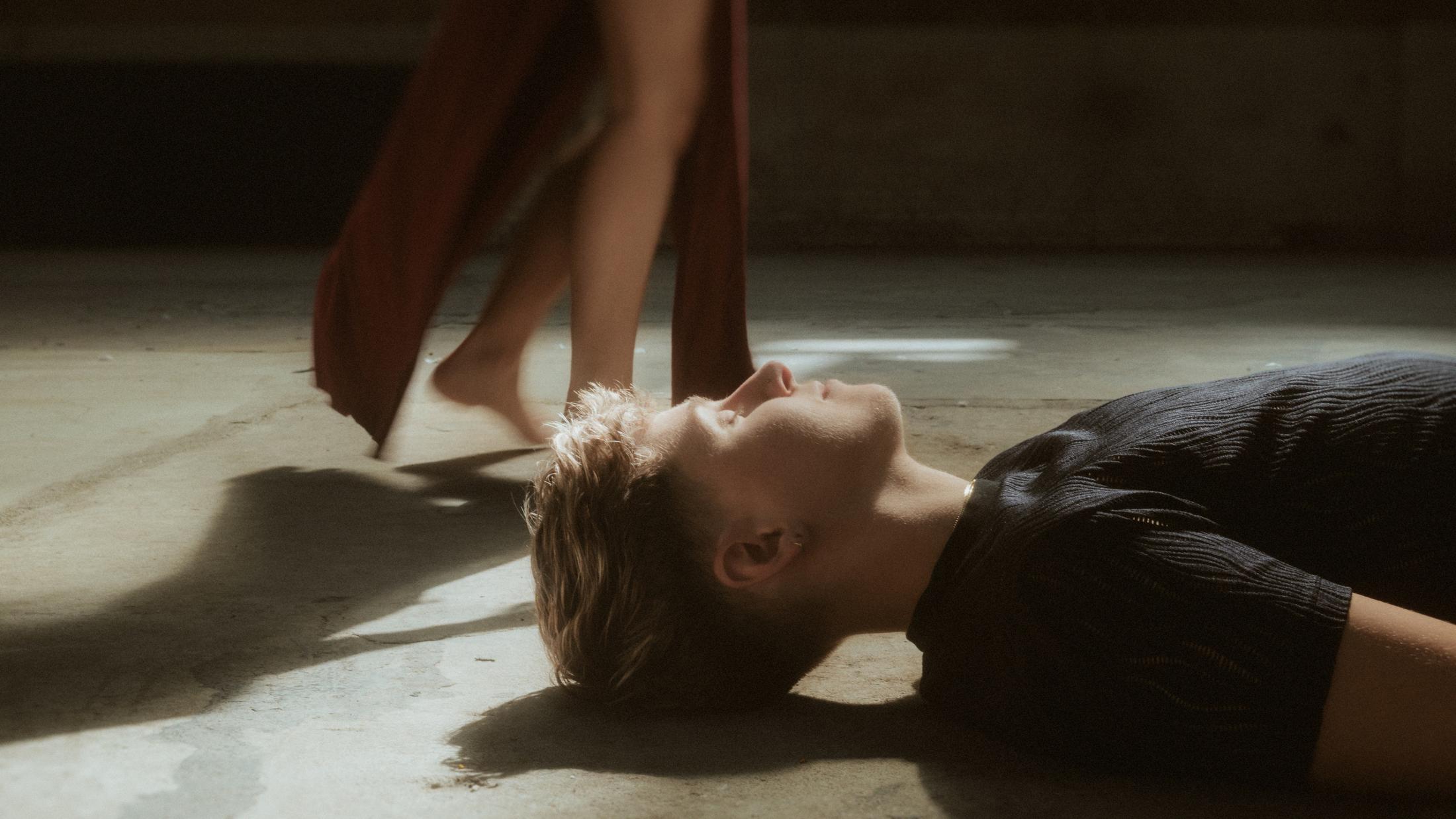 Noah lying on the concrete floor as a hard shaft of sunlight crosses their face.