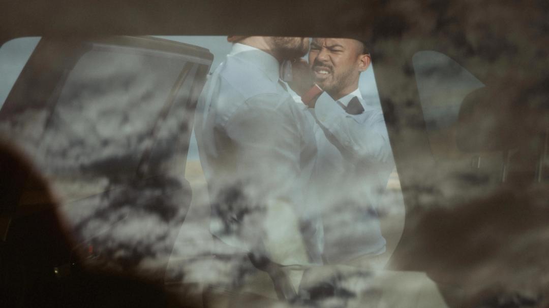 Kris and Ilya appear in a layered reflection through a car window.
