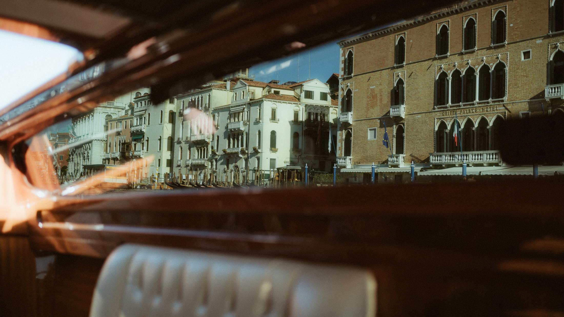 Venice is seen through the dark wooden frame of the boat during departure.