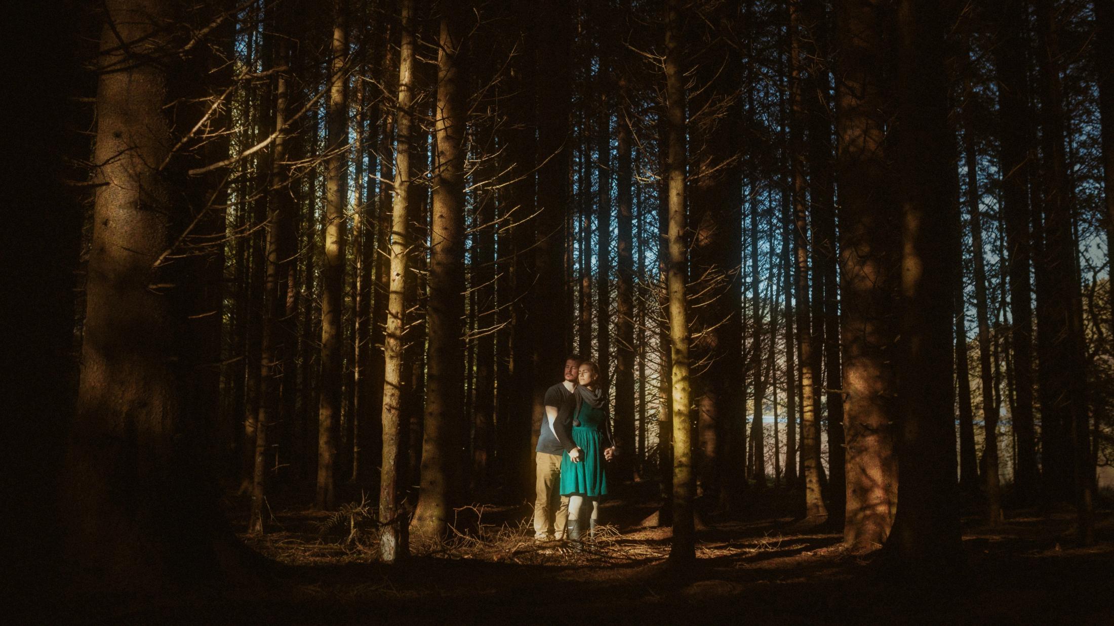 Jule und Rory stehen als kleine Gestalten in einem dunklen Kiefernwald.