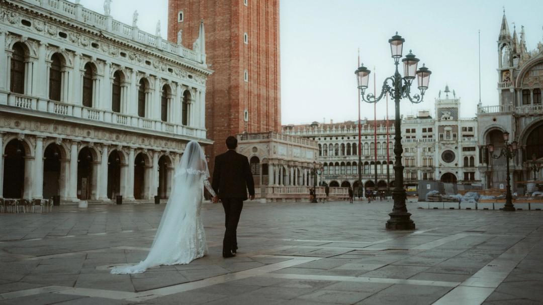 Newly married couple walking across an almost empty St Mark’s Square in Venice before sunrise