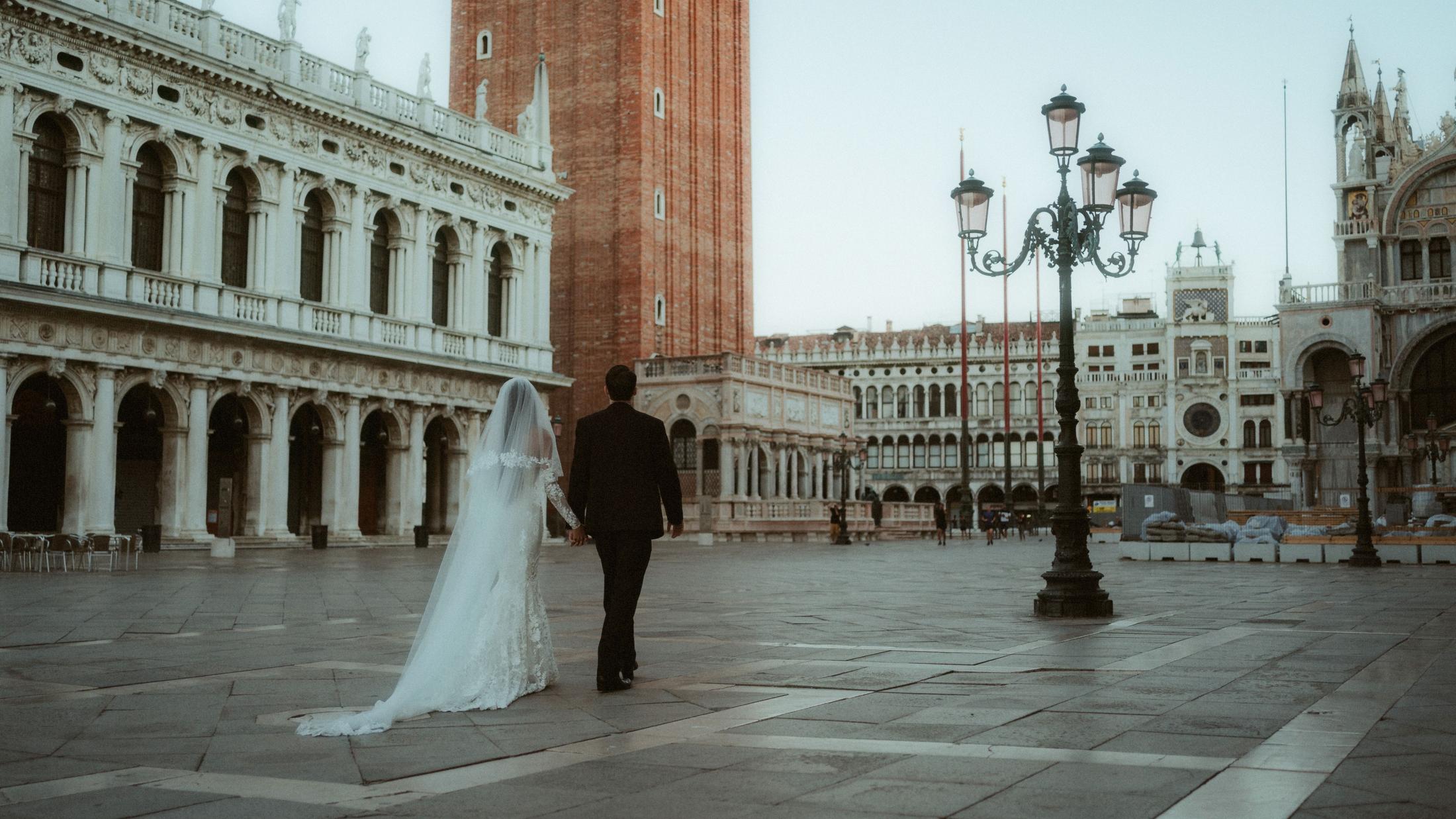 A newly married couple walks across an almost empty St Mark's Square in Venice.