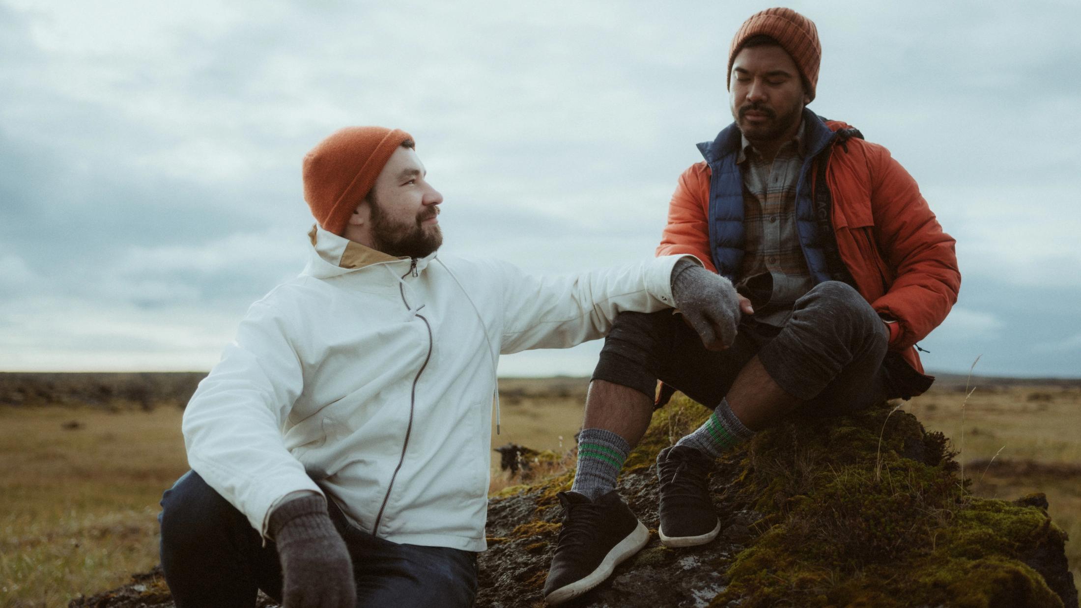 Kris und Ilya sitzen gemeinsam in ihren Outdoorjacken im Gras.