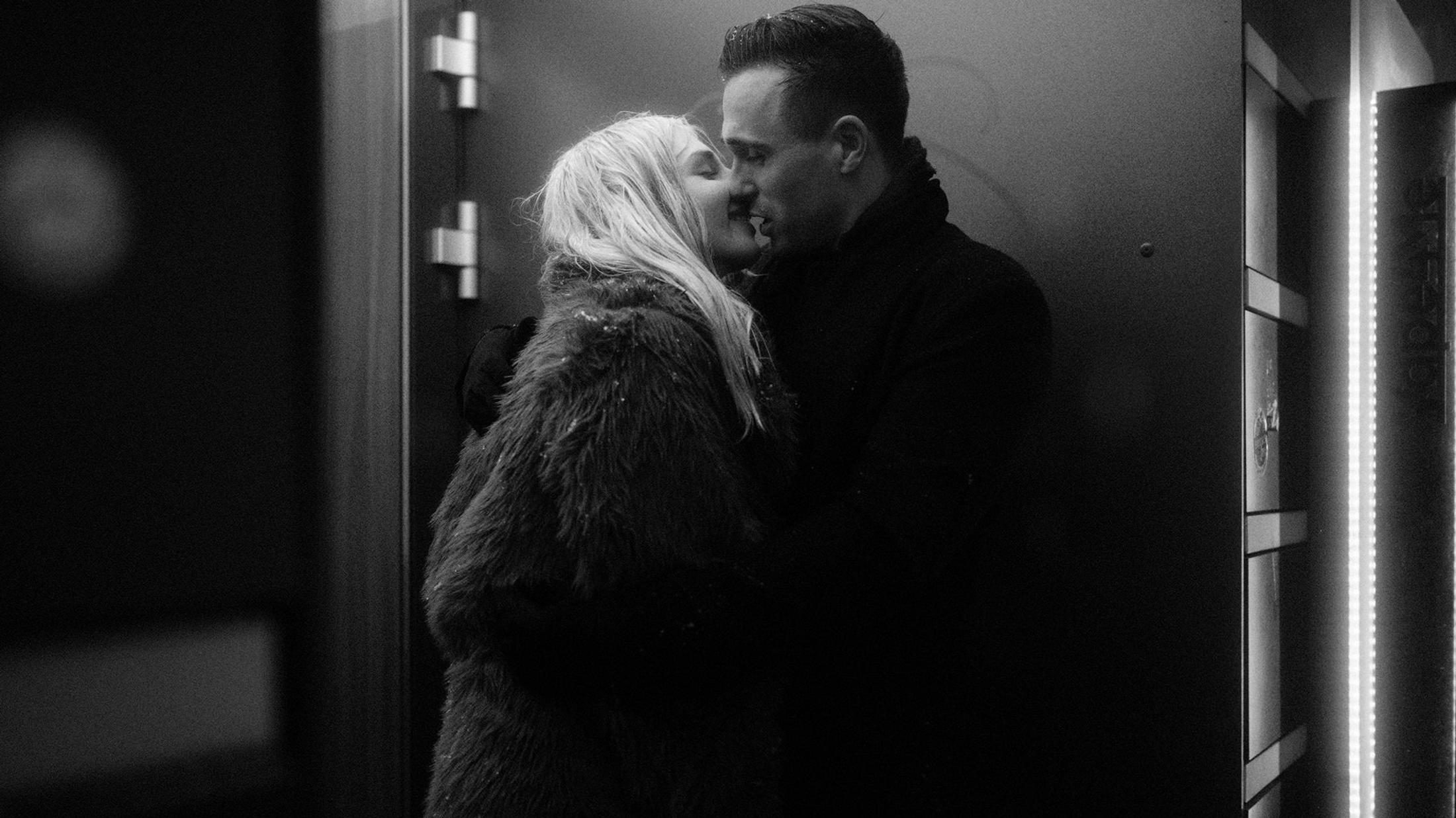 Lorelai and Steffen kiss beside a lit doorway on the Reeperbahn, in black and white.