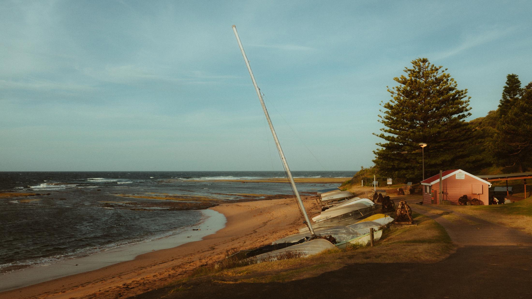 Wide view over a rocky Sydney beach with a small boatshed and ocean beyond