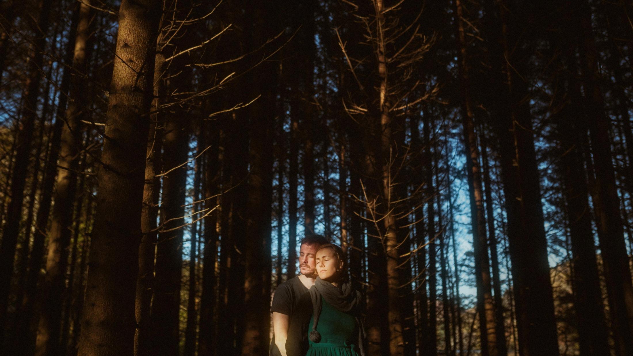 Jule und Rory umarmen sich dort, wo ein Lichtstrahl den Waldboden trifft.