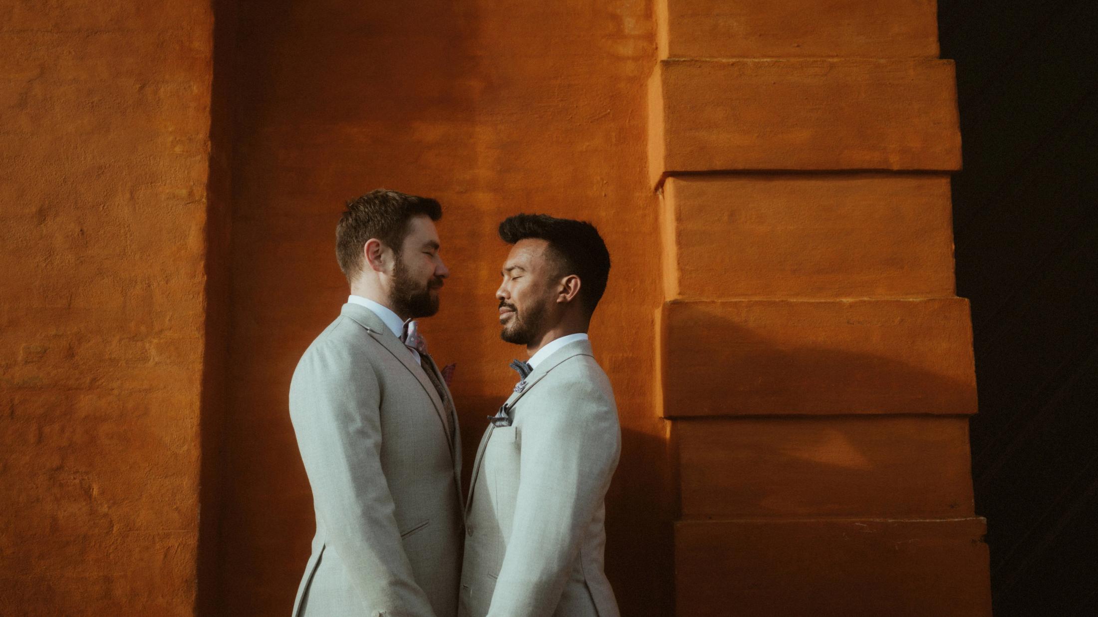 Kris and Ilya stand chest to chest in a narrow band of orange evening light.