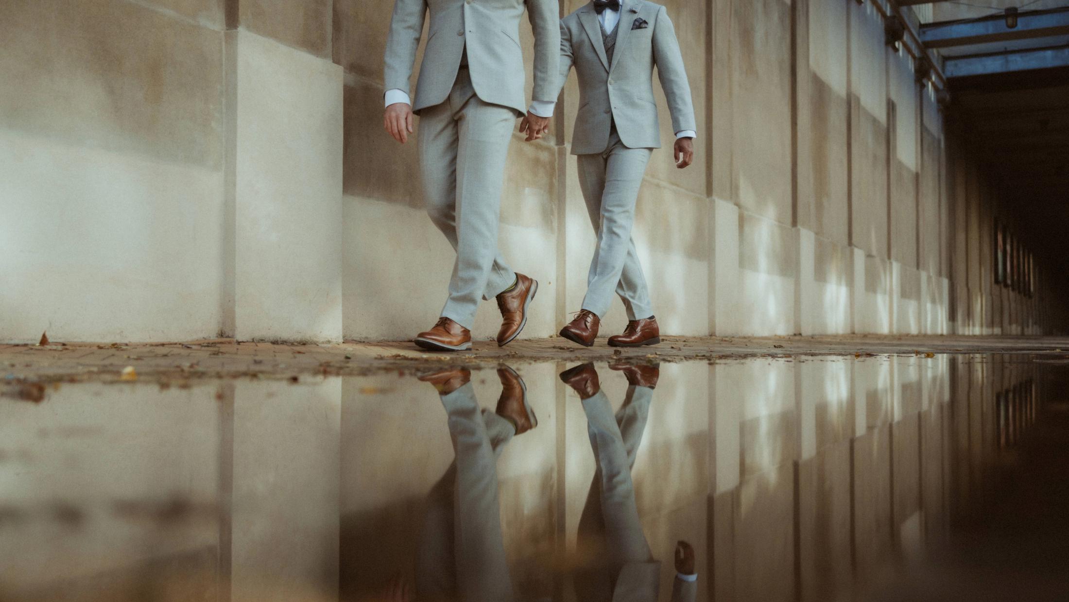 Kris and Ilya walk beside a long puddle that reflects their light suits.