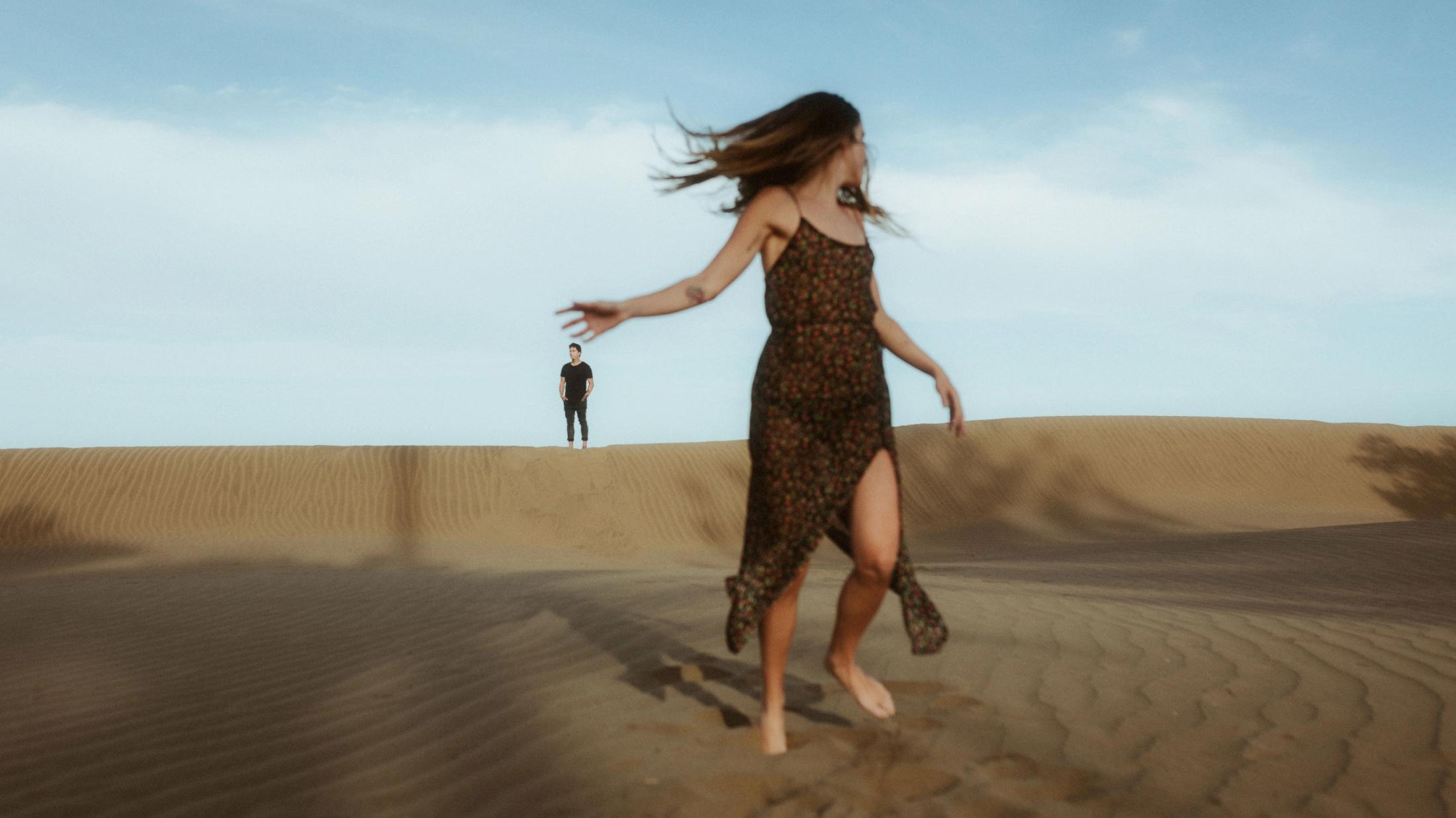 Detailaufnahme ihrer Fingerspitzen, die sich fast berühren, Sand im Hintergrund.