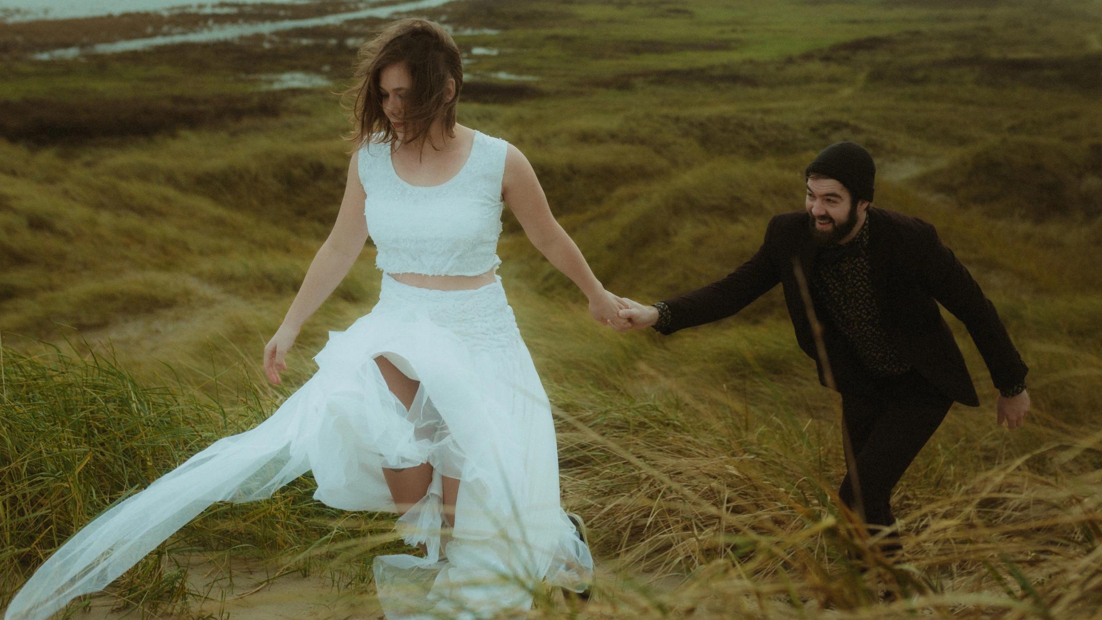 Anni runs ahead through tall grass while Daniel holds her hand.