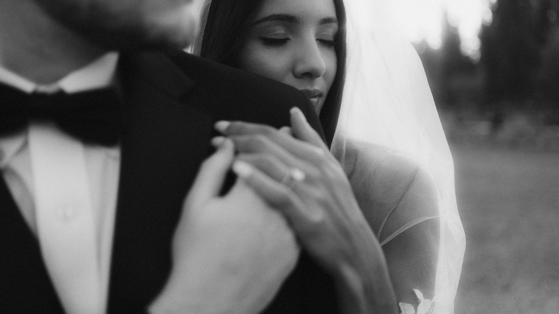 The bride closes her eyes against her partner's shoulder, her hands resting on his jacket.