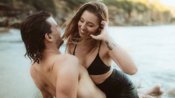 Woman laughing and playing with her hair in the ocean while her partner watches, Sydney, Hafenliebe