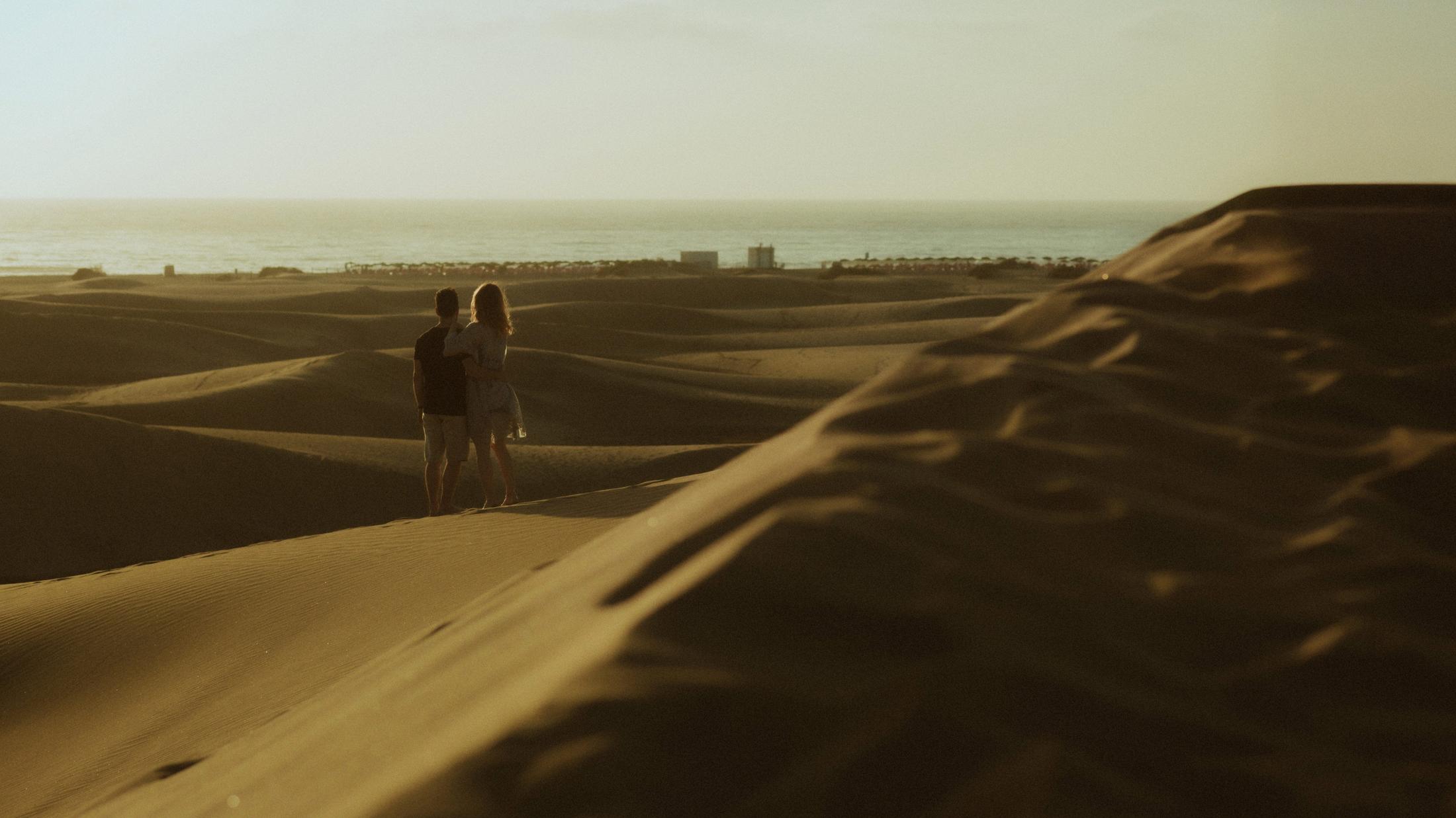 The couple looking across the dunes toward the Atlantic and distant buildings.