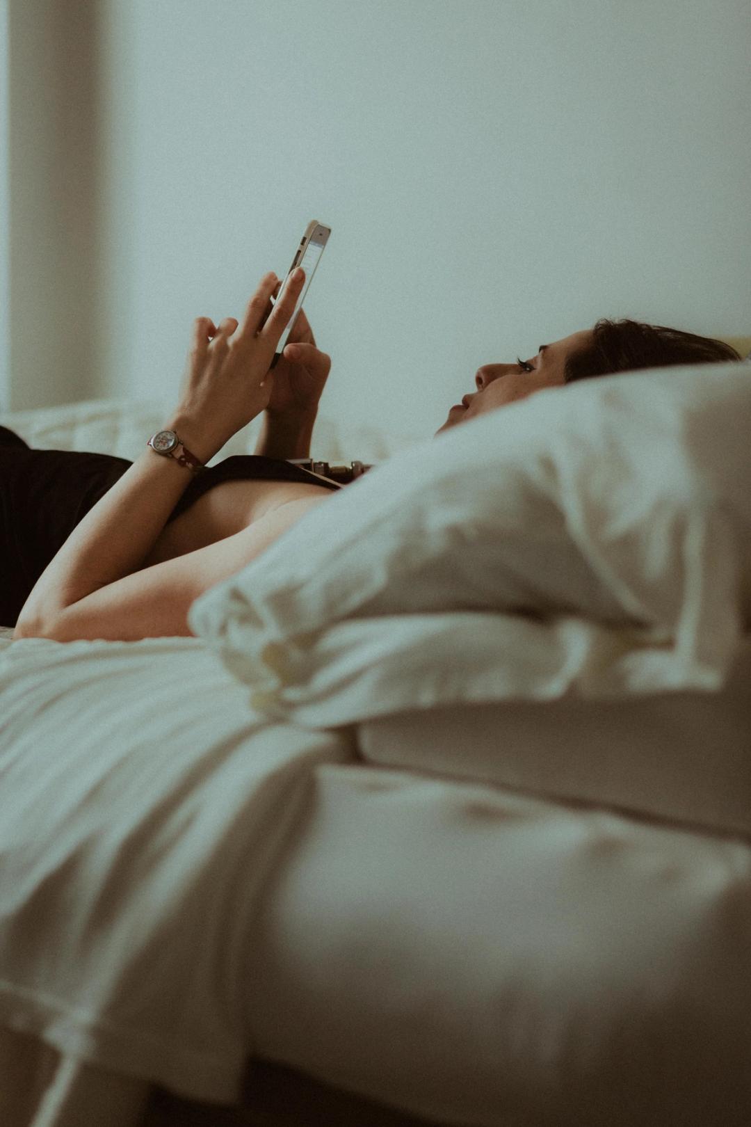 Maya reclining beneath a white duvet with one hand raised.