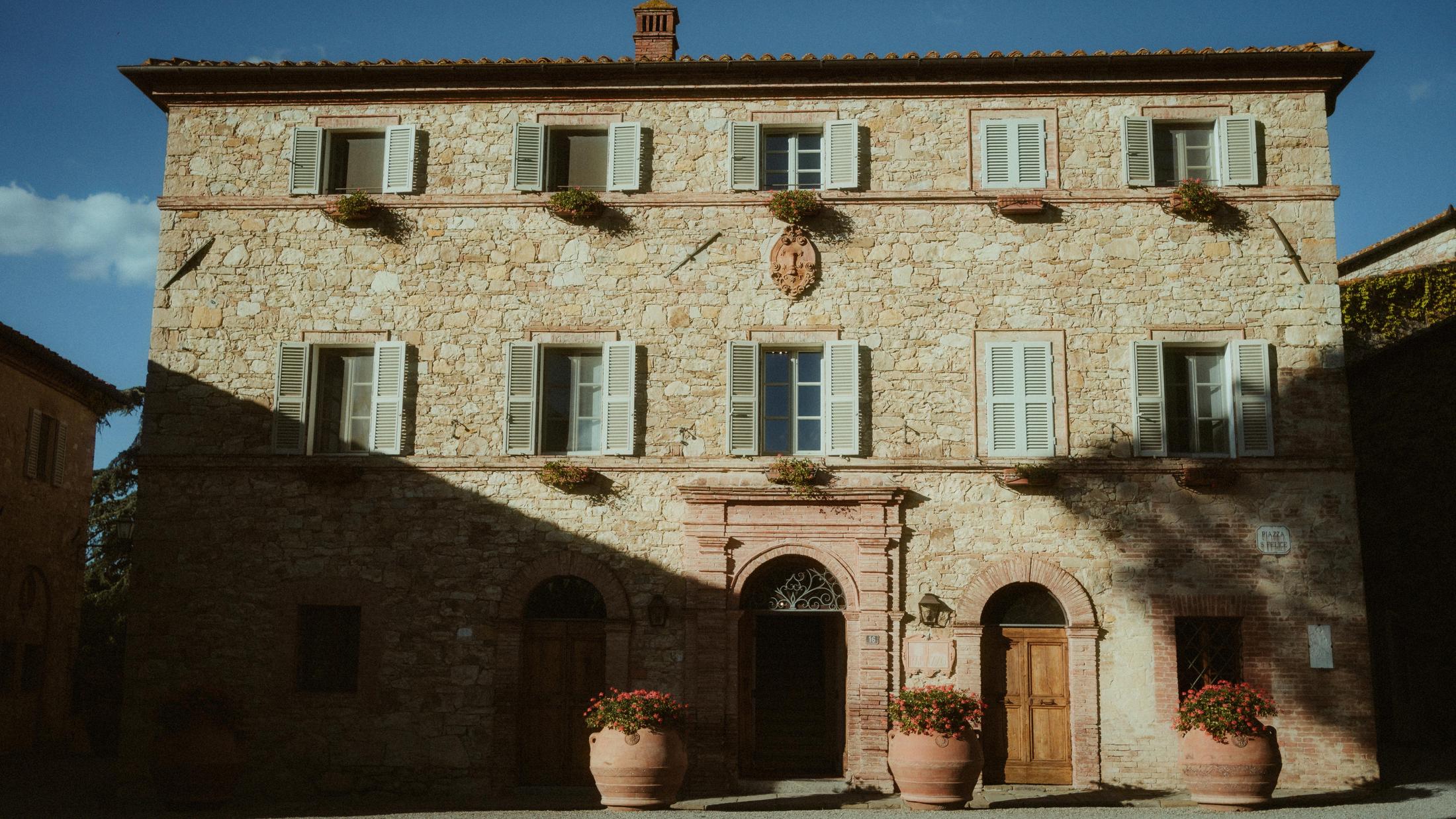 Frontal view of a symmetrical Tuscan stone house beneath a blue sky.