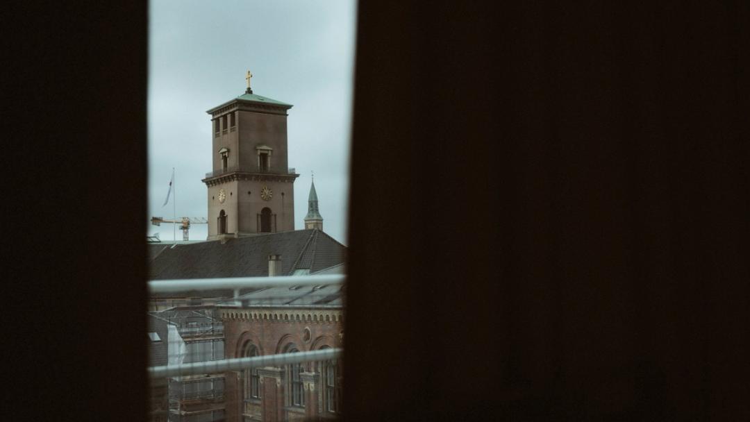 Copenhagen City Hall's clock tower is framed by dark hotel curtains.