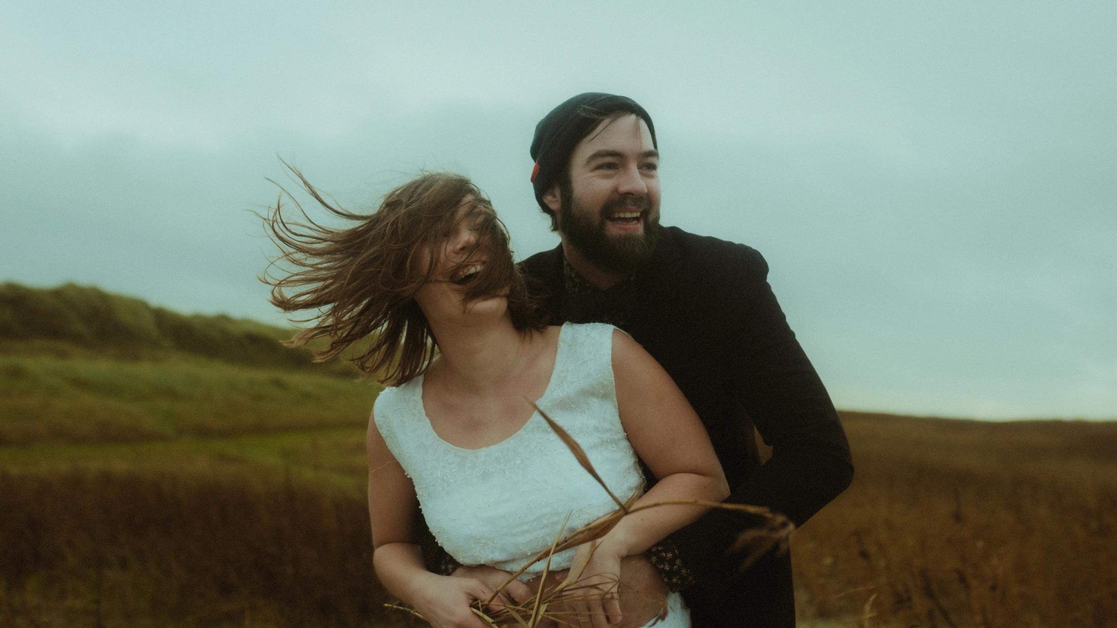 Anni and Daniel laugh together as the wind blows her hair sideways.