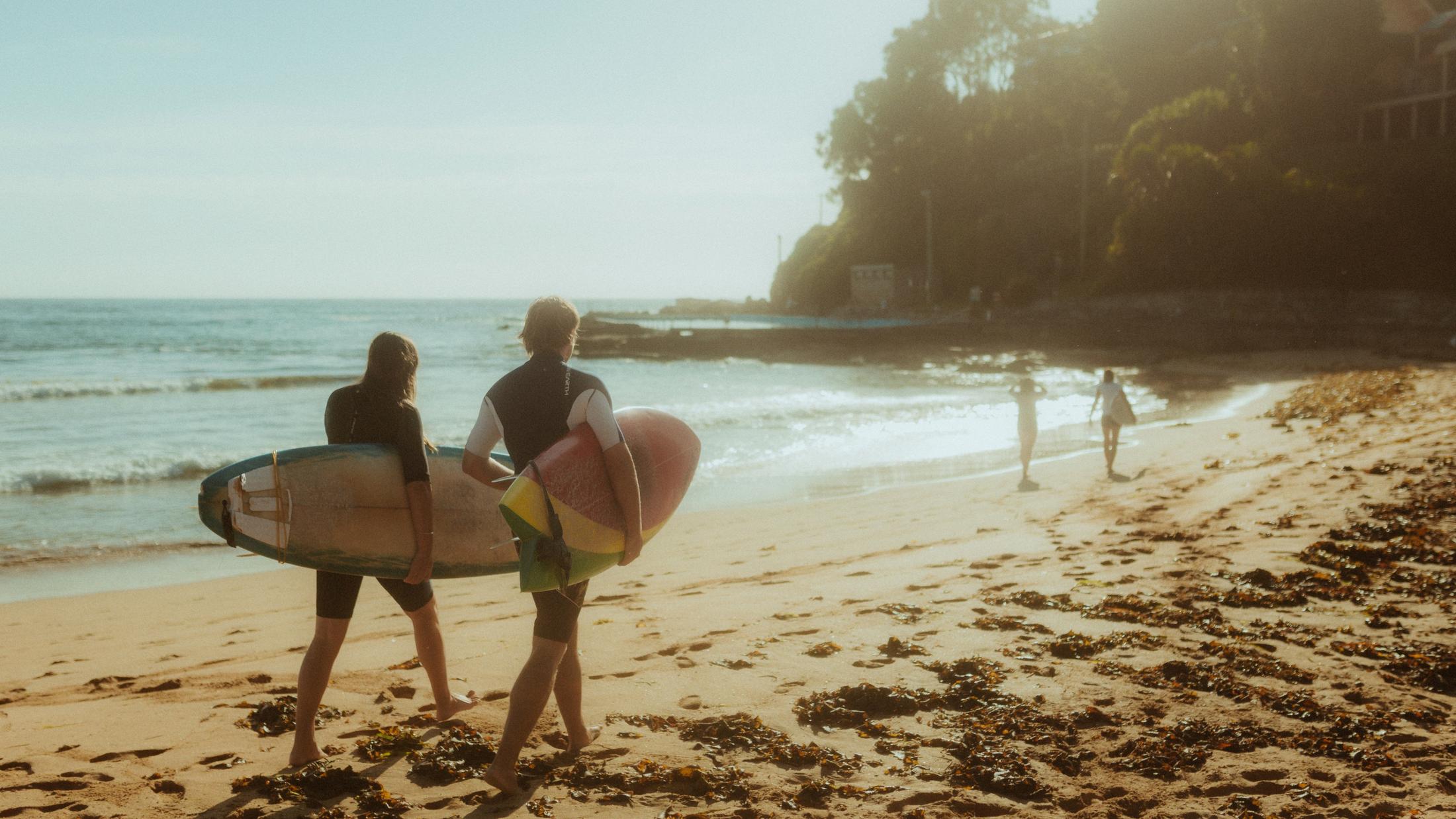 Petra and Roman walking toward the water with surfboards