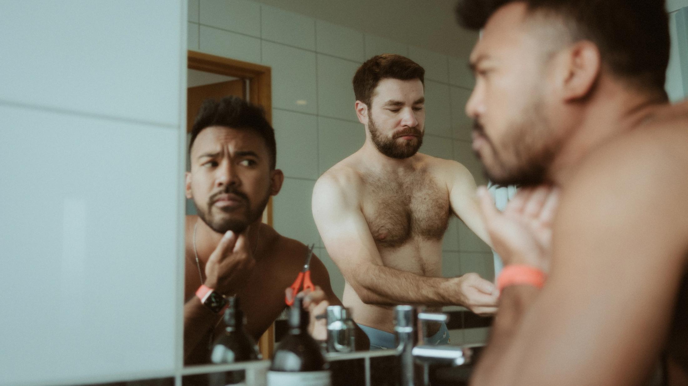 Kris looks into the bathroom mirror while Ilya gets ready behind him.