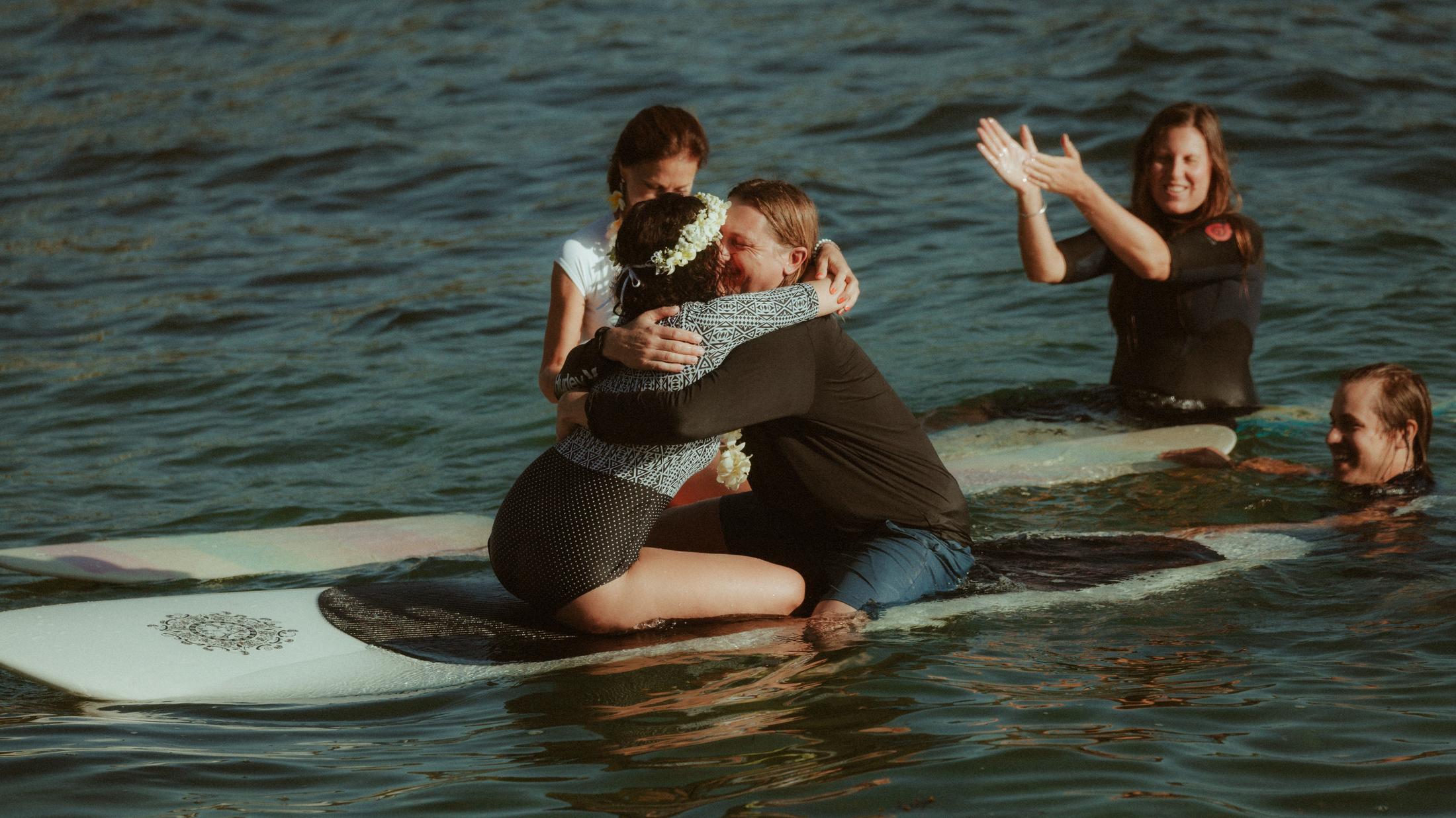 Petra and Roman embracing on their boards while witnesses watch from the stone pool
