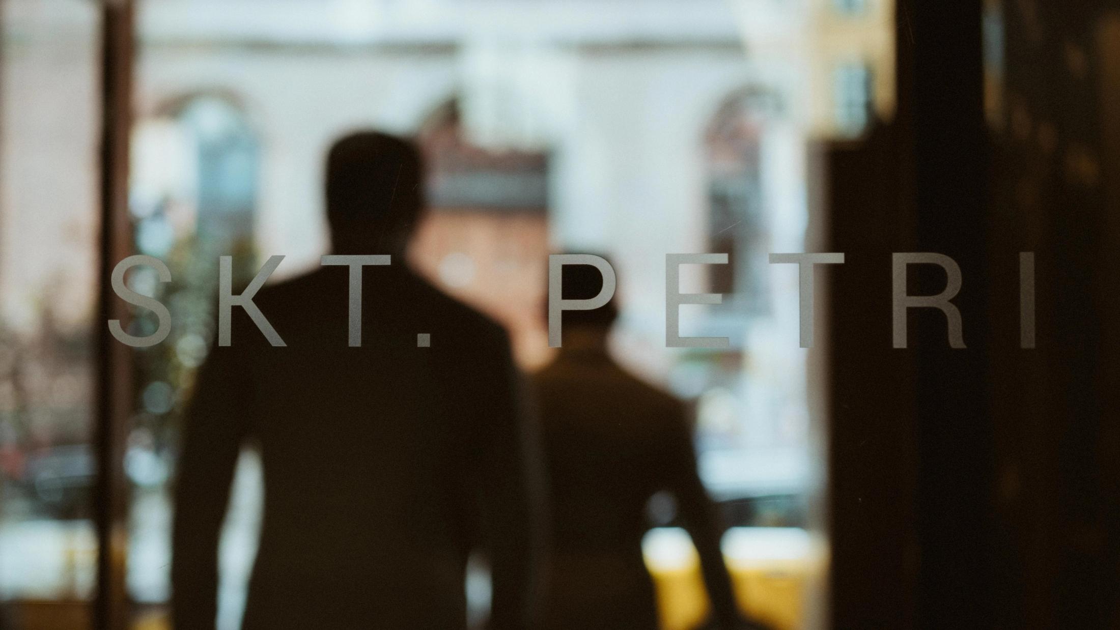 Kris and Ilya are reflected in the glass entrance of Hotel Skt. Petri in Copenhagen.