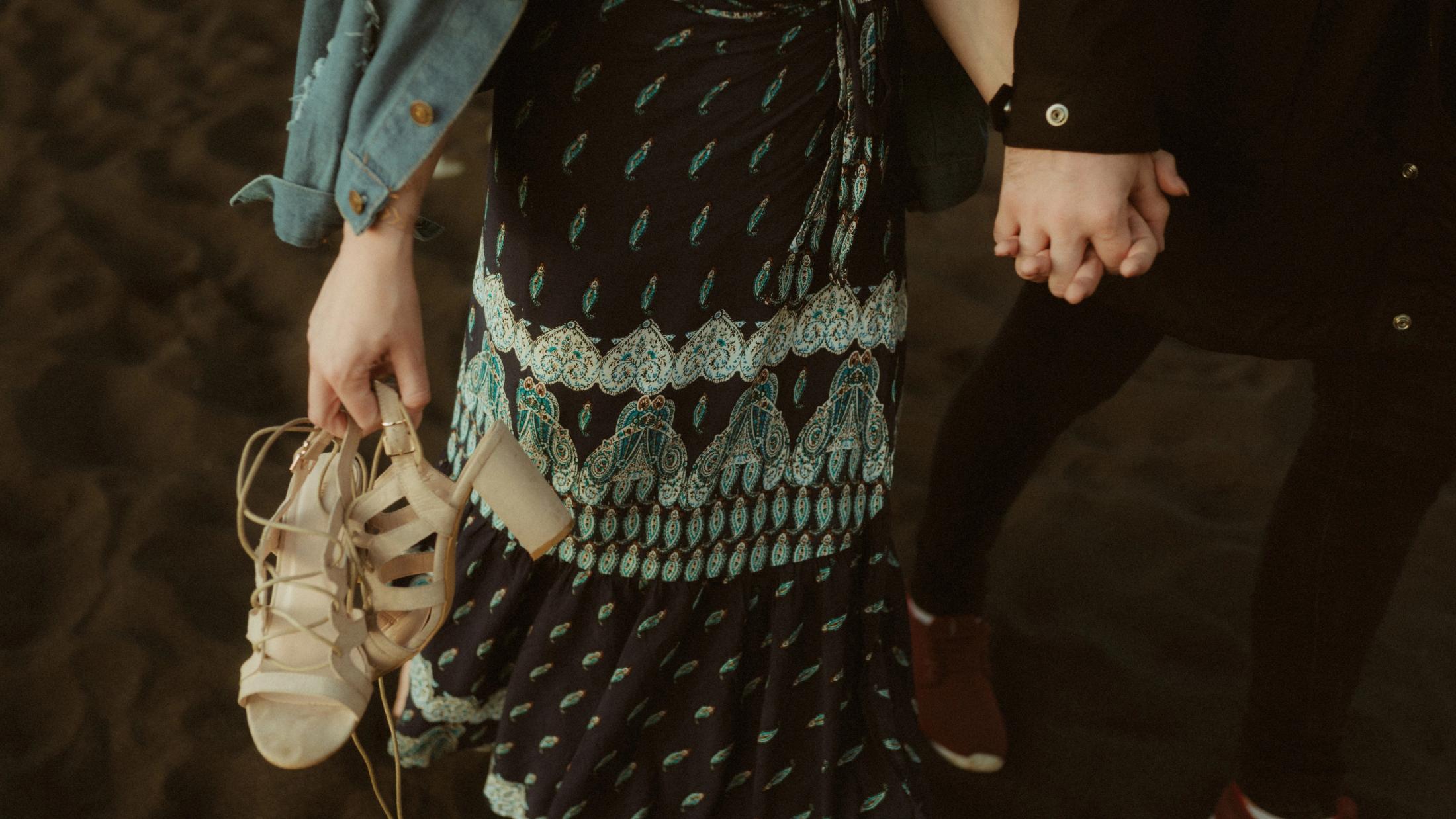 Two guests hold hands while carrying their shoes across the black sand.