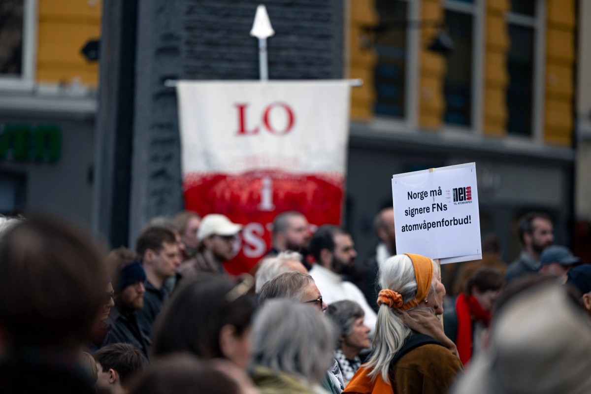 Fra markeringen ved Fredsmonumentet. Folk står i en gruppe, en håndplakat som sier "Norge må signere FNs atomvåpenforbud" er i fokus. Foto: Olav Helland 
