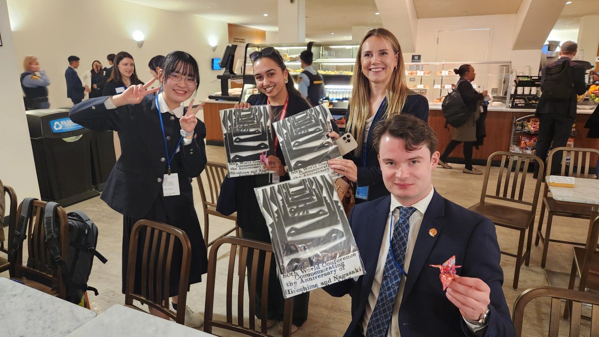 Fire unge mennesker smiler mot kamera. De holder oppe papirtraner og t-skjorter fra Hiroshima Nagasaki Peace Messengers. 