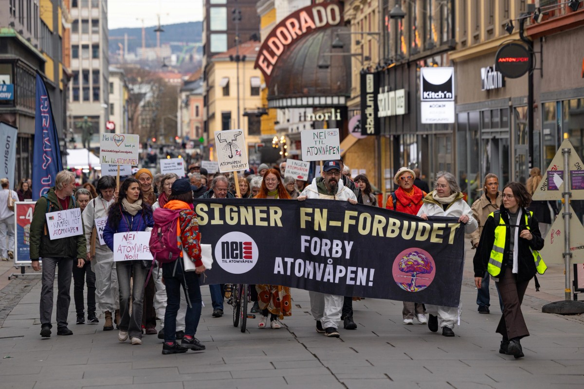 Aktivistene marsjerer mot Stortinget bak et banner som sier "Signer FN-forbudet. Forby Atomvåpen!". Foto: Olav Helland 