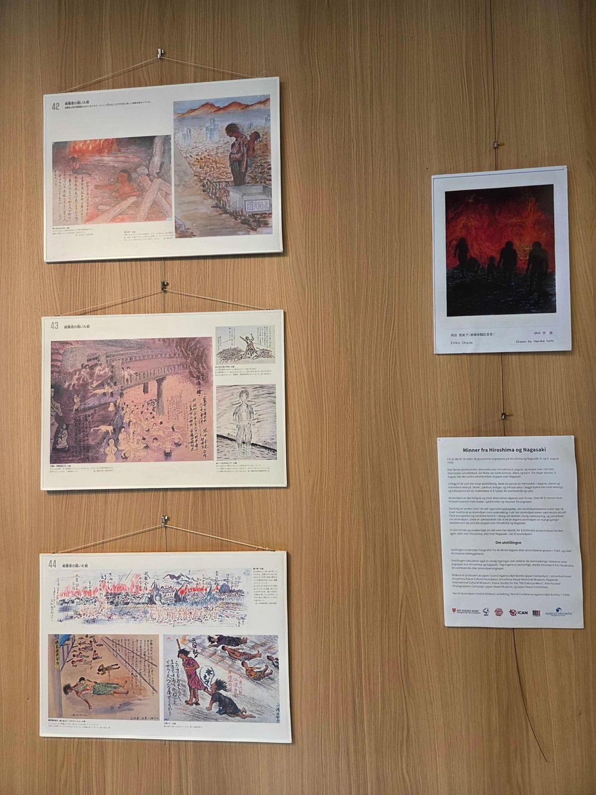 På bildet er det fire kunstverk med vitnesbyrd fra atomvåpenangrepet på Hiroshima og Nagasaki, hengende på en trevegg.