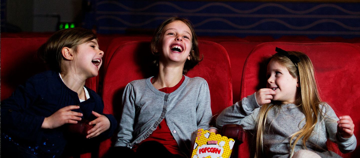 3 jenter på kino som spiser popkorn og ler og smiler.
