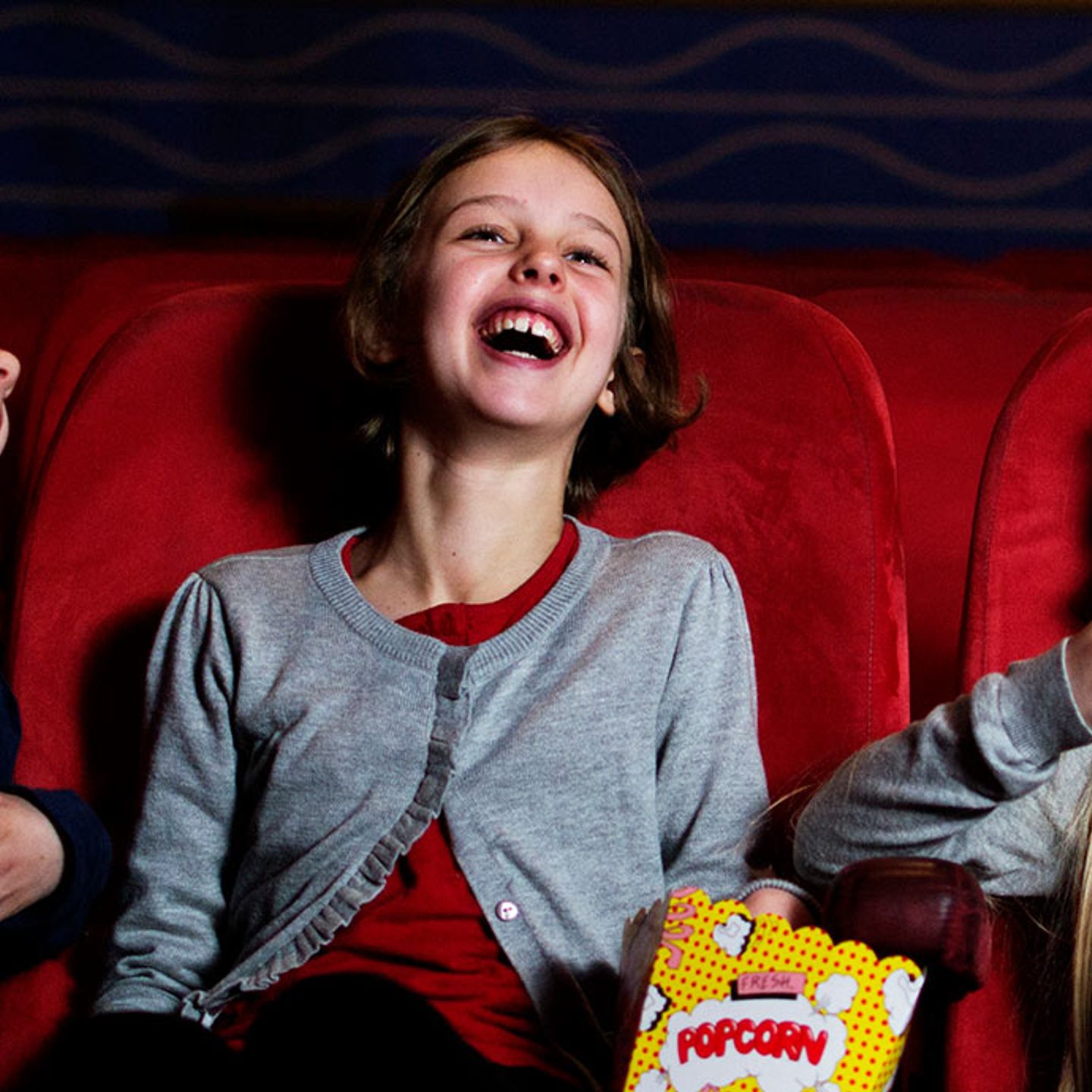3 jenter på kino som spiser popkorn og ler og smiler.