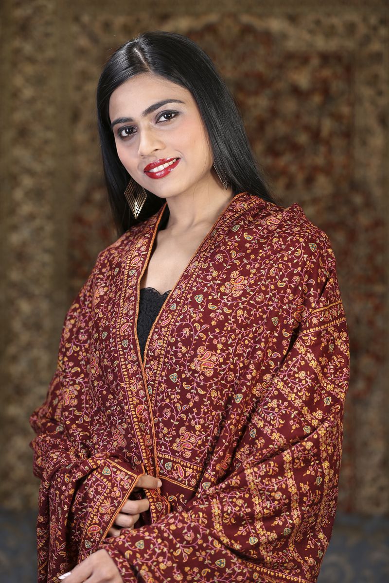 A maroon pashmina shawl with intricate sozni floral embroidery, worn by a model