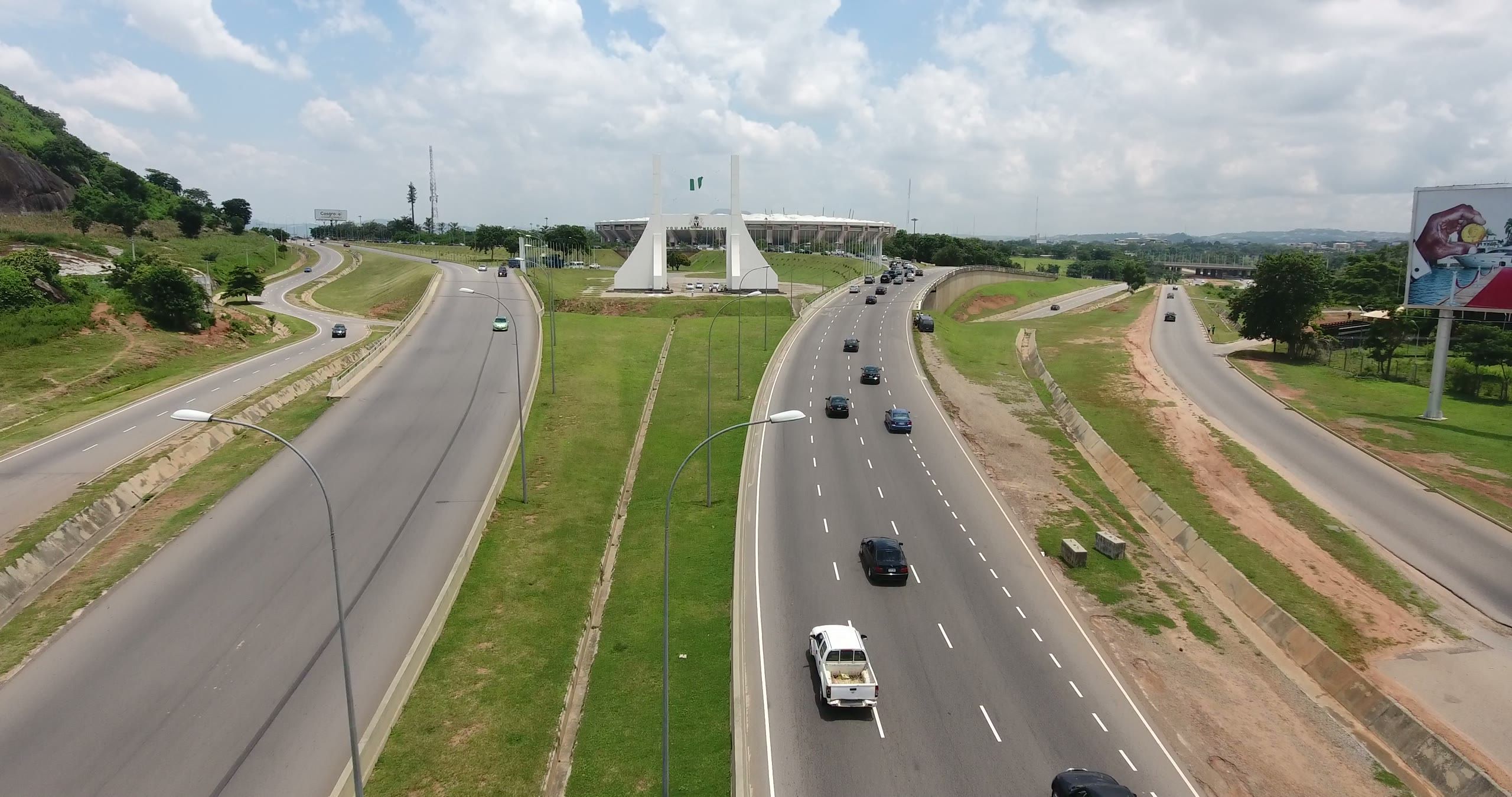 Aerial view of a dual carriageway leading into Abuja past a roadside monument