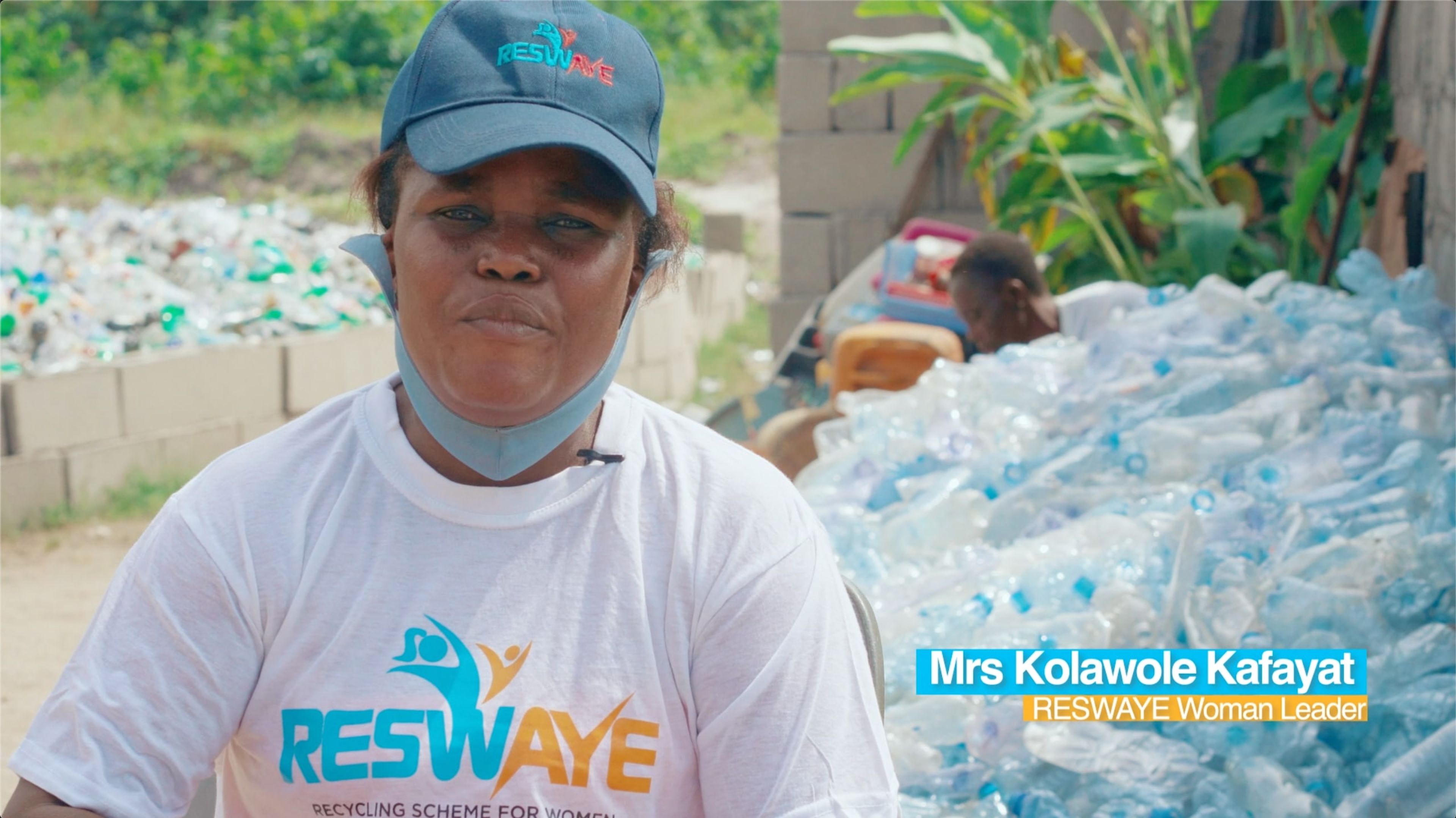 A woman in a Reswaye cap and T-shirt beside sacks of collected plastic bottles