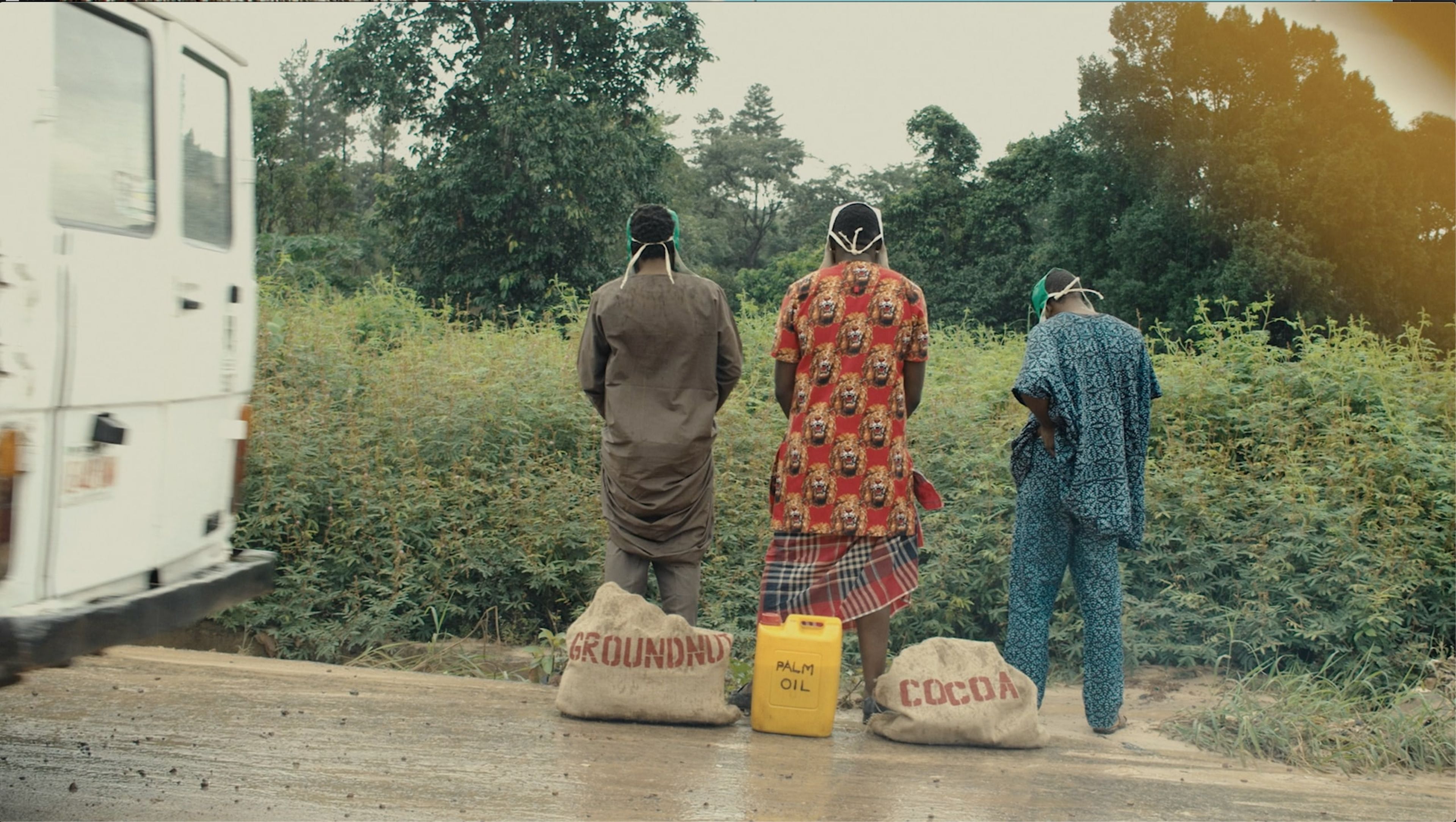 Three people carrying sacks of groundnut and cocoa at the roadside beside a truck