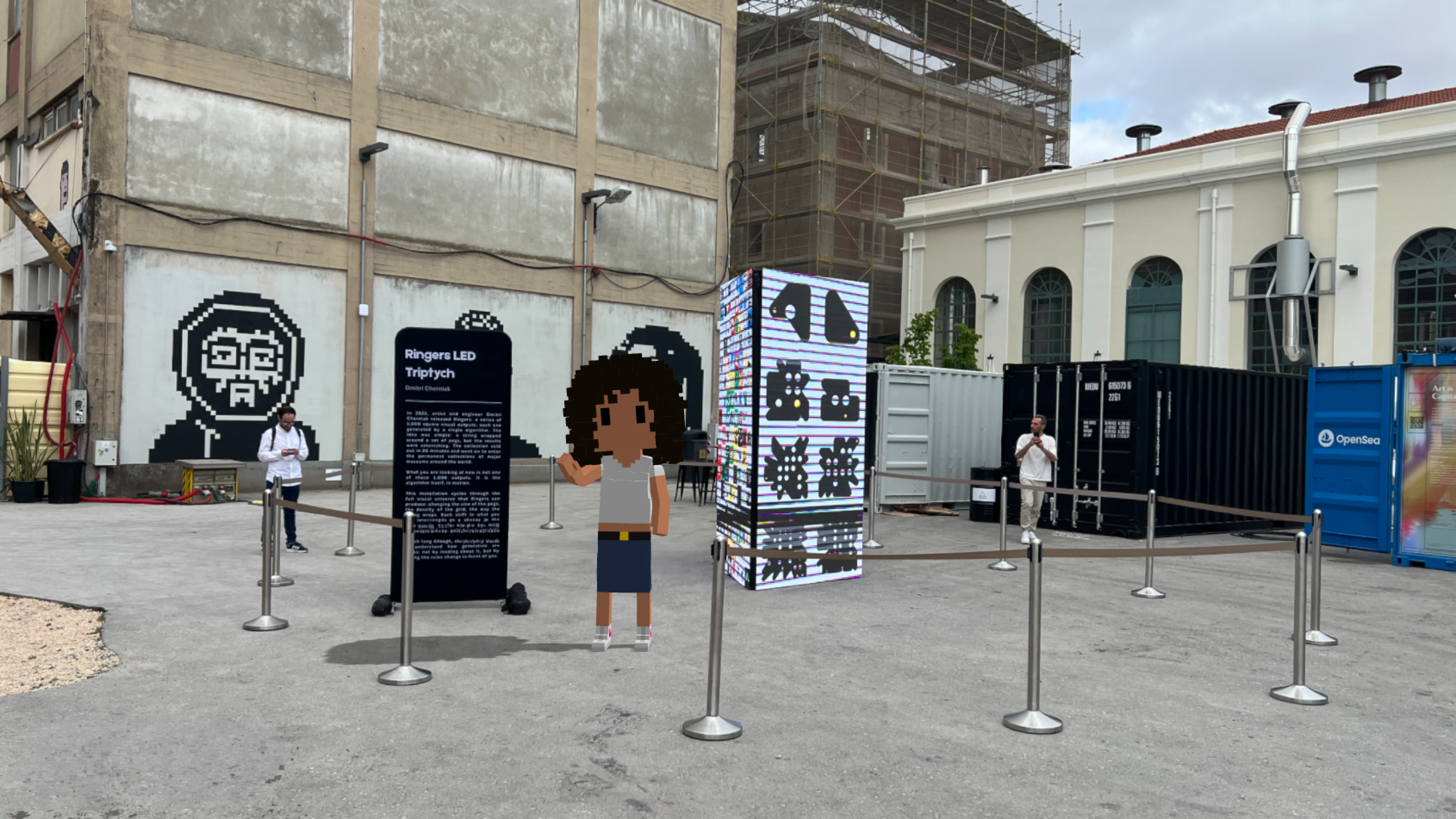 Midl standing in NFC's main plaza between Normies murals, an OpenSea container, and a Dmitri Cherniak Ringers installation.
