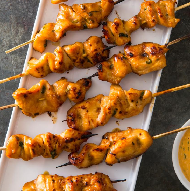 Grilled chicken satay skewers on a platter with peanut sauce