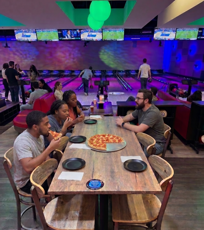 Guests sharing a pizza at a table beside the bowling lanes