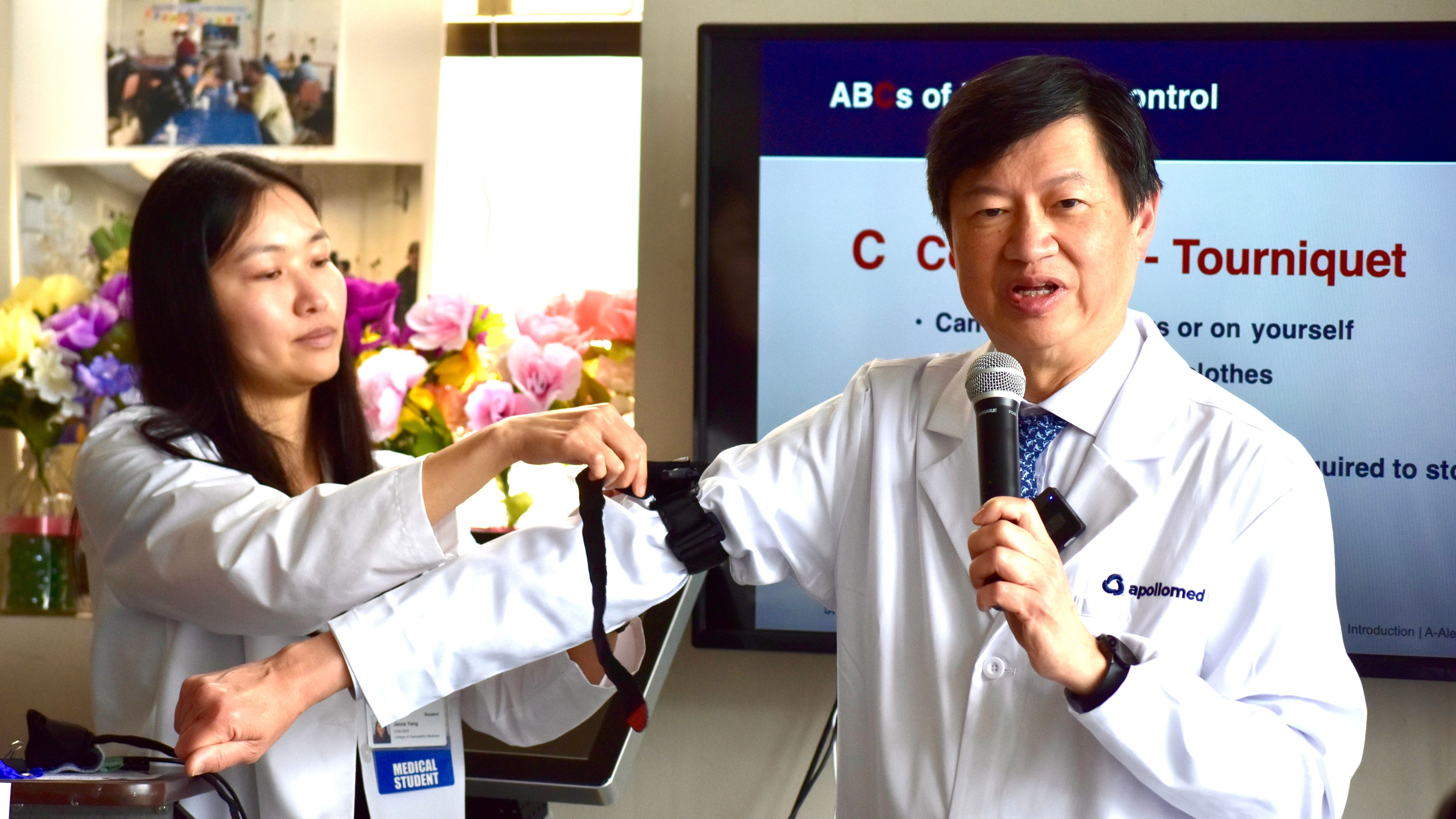 Medical school student Janna Yang (left) ties a tourniquet around Dr. Edmund Tsoi’s upper arm that can be more effectively to stop the bleeding. Photo by Portia Li