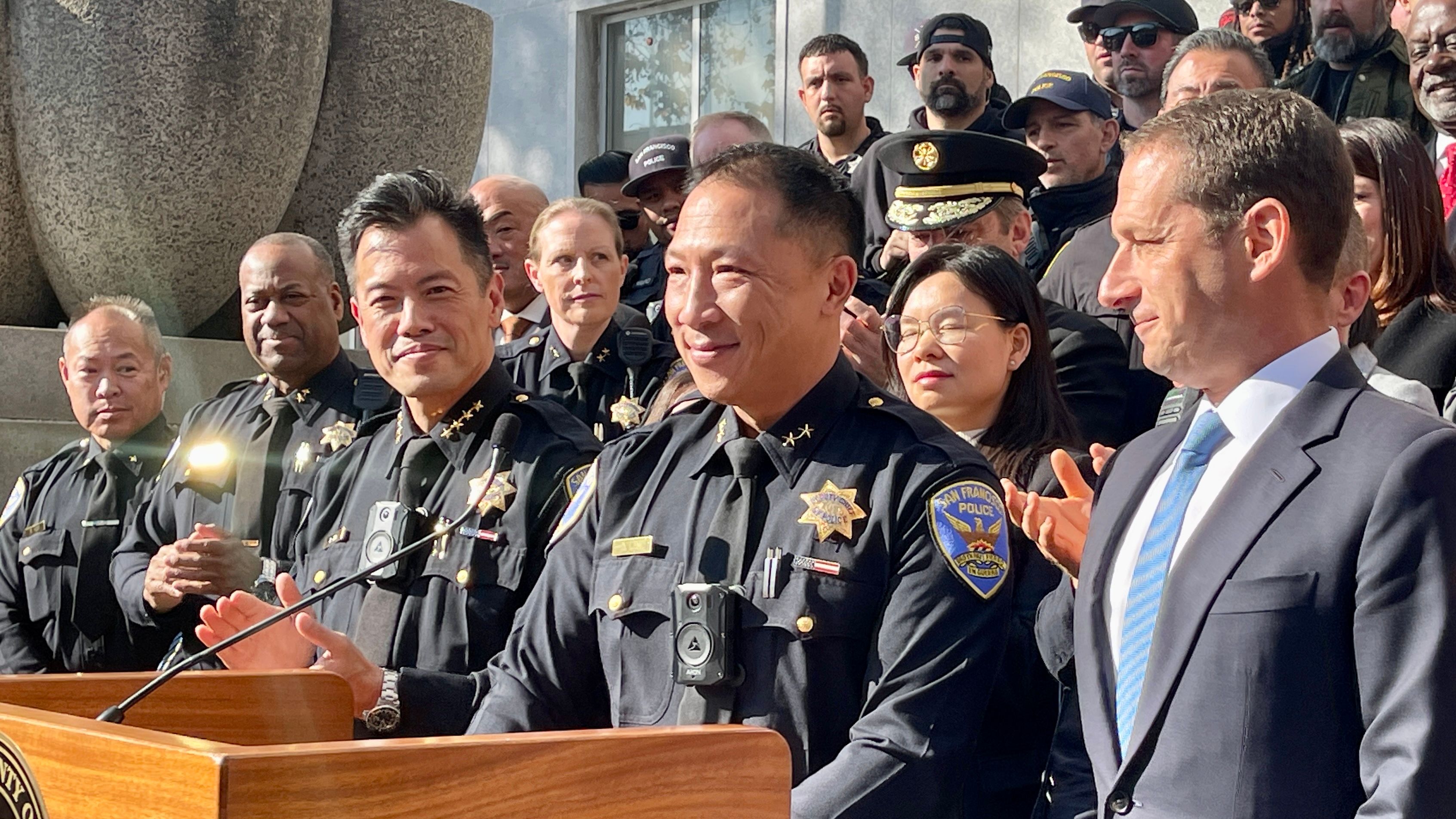 Fellow officers gather on the steps of Hall of Justice to congratulate incoming Police Chief Derrick Lew (2nd from far right in front row ) when Mayor Daniel Lurie (1st from far right) announces the appointment for the San Francisco Police Department. Interim Chief Paul Yep (center in front row) applauds for the appointment. Photo by Portia Li