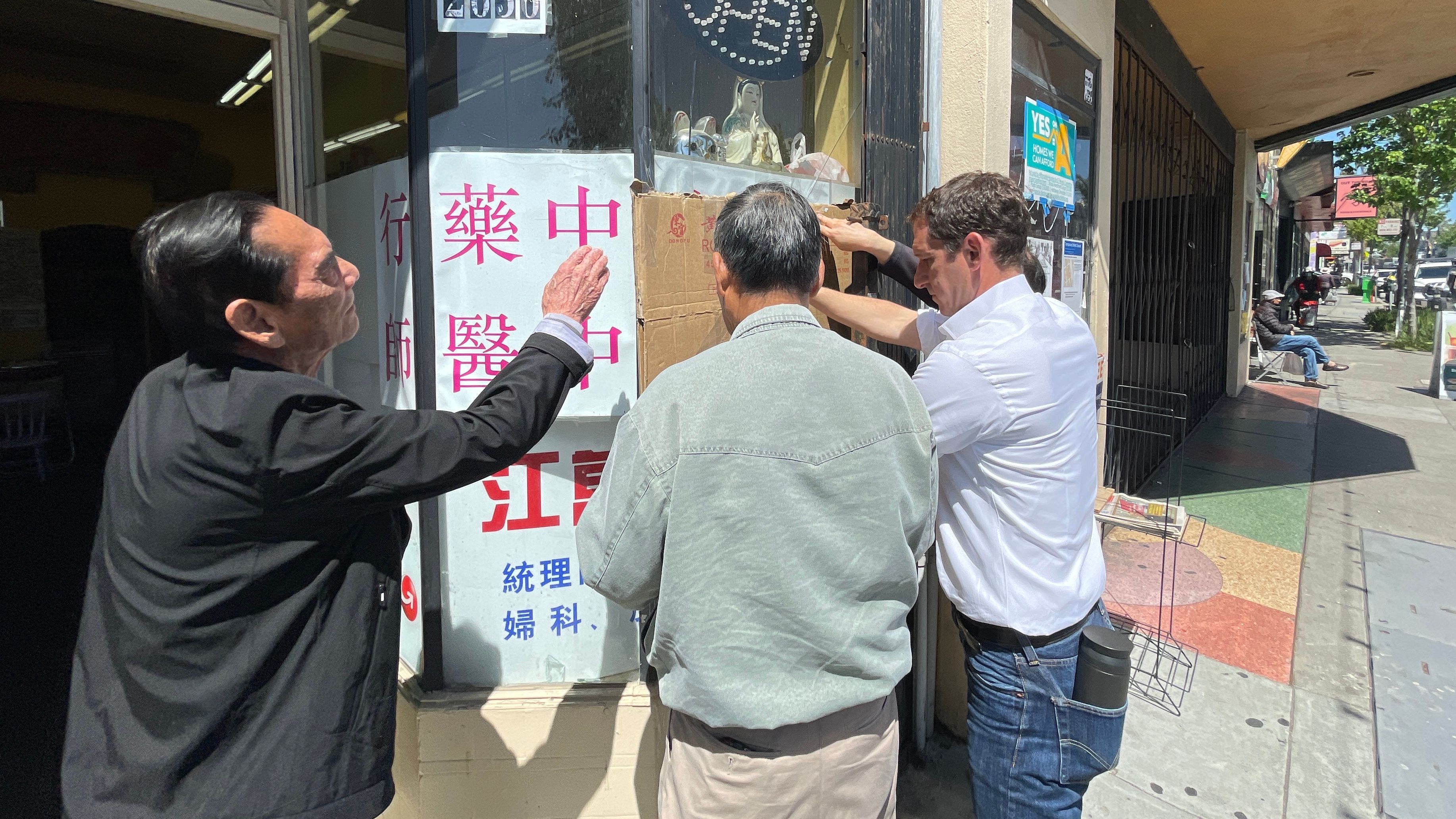 Mayoral candidate Daniel Lurie joins Chinese medicine doctor Wan Chen Jiang and his friends to put up cardboard covering the smashed window. Photo by Portia Li