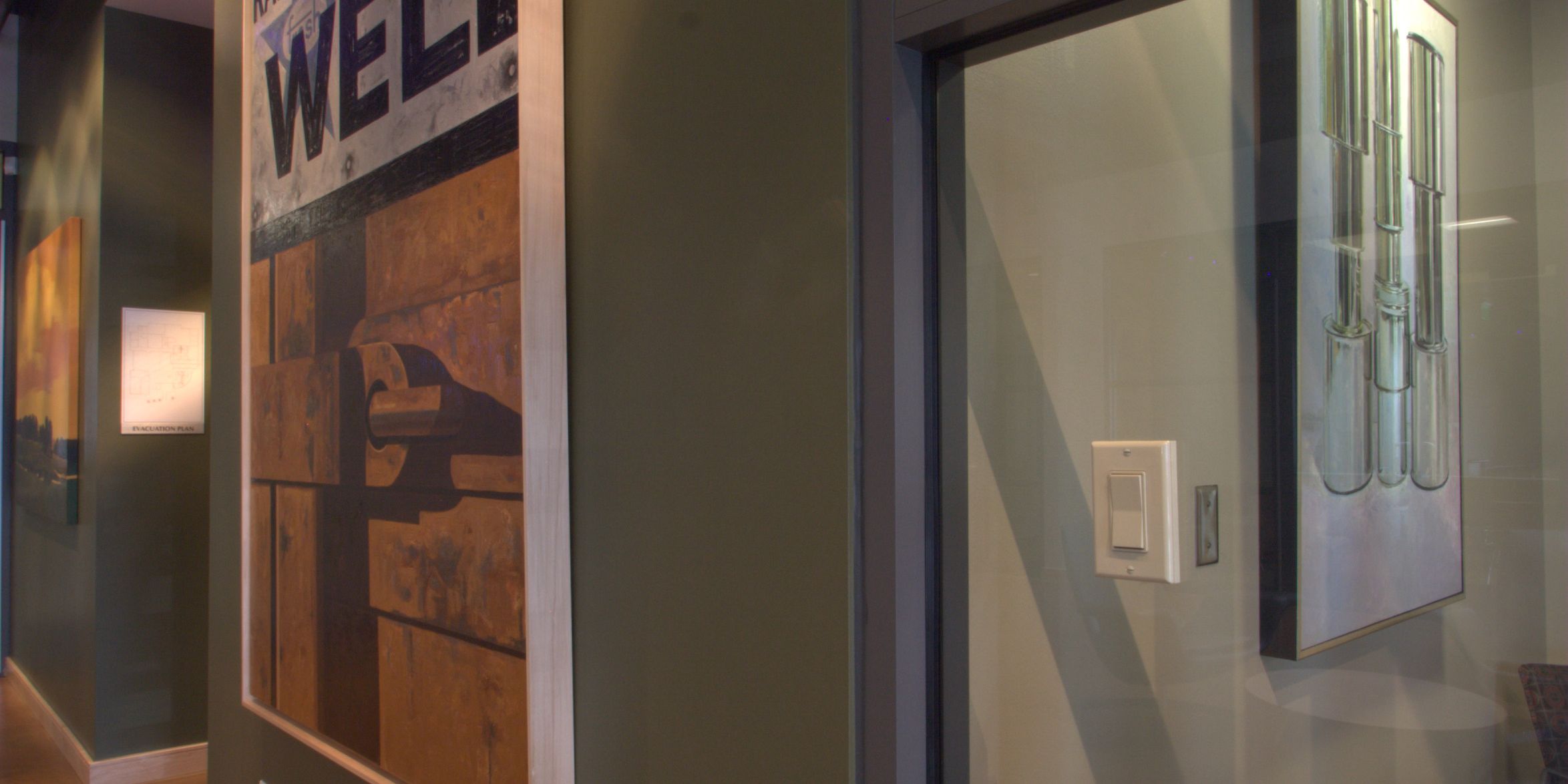 A hallway with a dark green wall displaying a large "Radiator Stop Well" sign artwork, a polished brown floor, and a glass partition to an adjacent room.