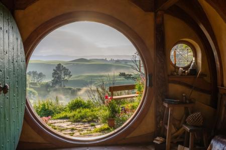 View through the round door of a hobbit hole over misty green hills at the Hobbiton Movie Set