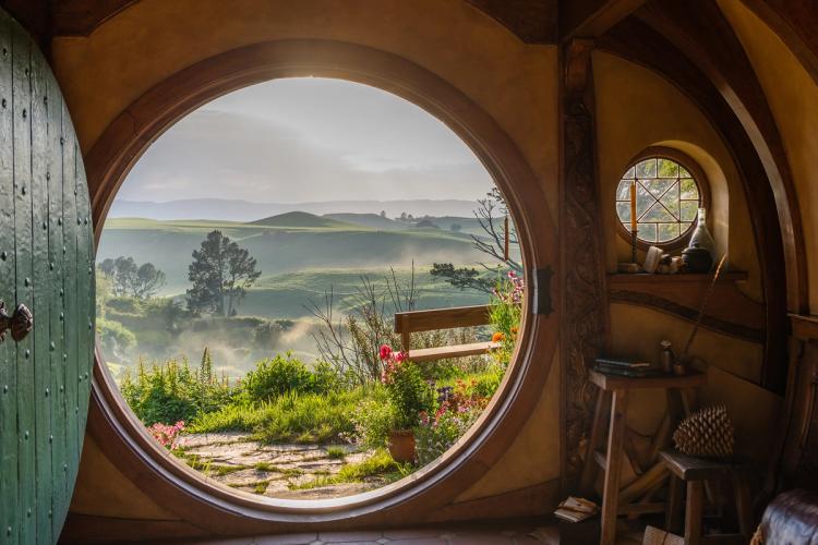 View through the round door of a hobbit hole over misty green hills at the Hobbiton Movie Set