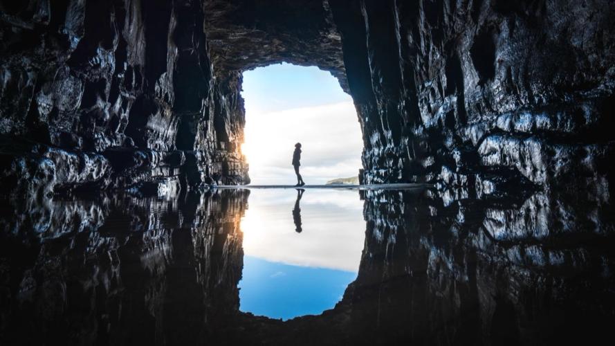 Person standing inside a cave with water on the ground
