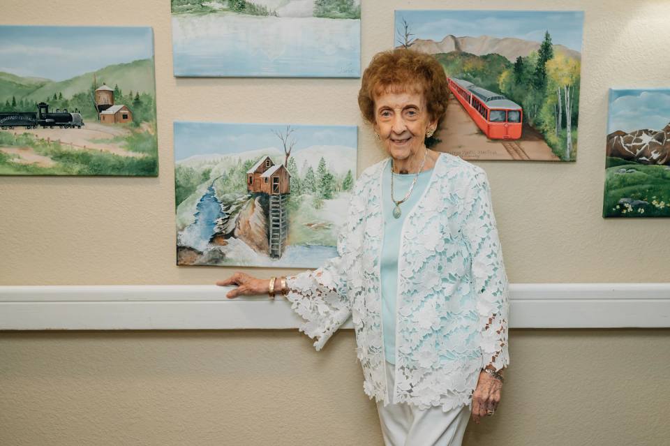 Golden Pond resident posing in front of her watercolor train and mountain paintings