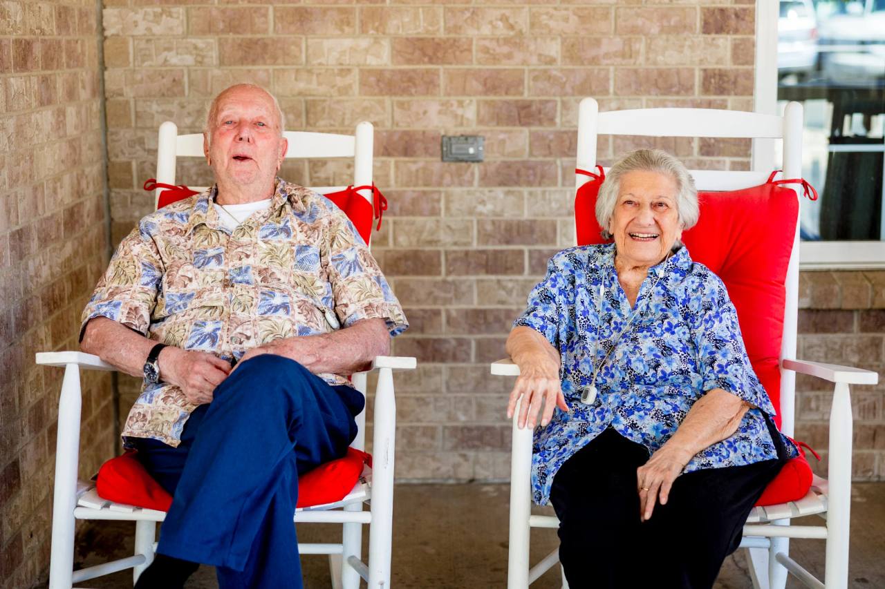Gardens at Columbine residents laughing in white rocking chairs on the brick porch