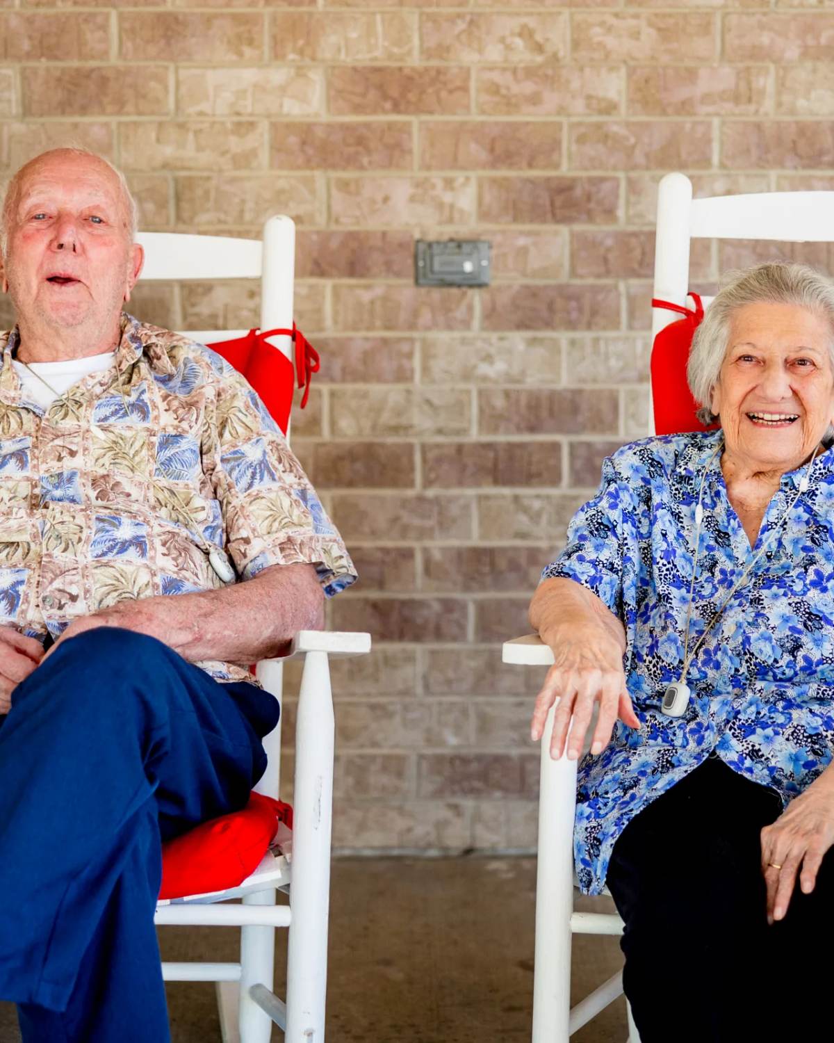 Gardens at Columbine residents laughing in white rocking chairs on the brick porch